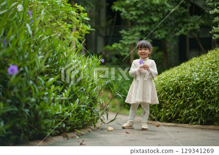 happy toddler girl in white dress with Ruellia simplex or Mexican petunia flower in garden 129341269