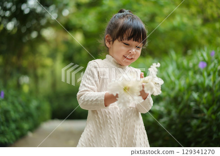 happy toddler girl in white dress with dolichandrone serrulata flower in garden 129341270