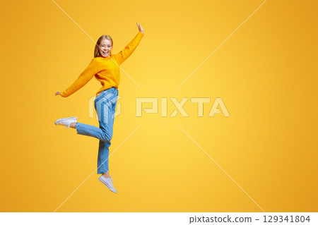 Be yourself. Pretty young girl jumping in air and laughing on orange background, free space 129341804