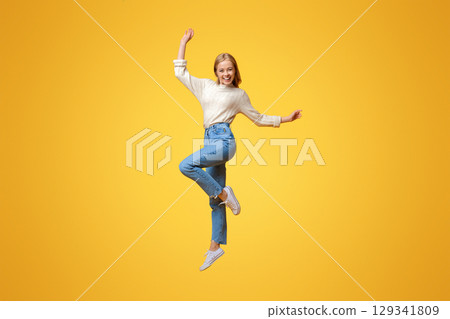 Happy teen girl having fun, jumping on orange studio background with copy space 129341809