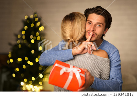 New Year surprise. Man making silence gesture and embracing woman, giving present 129341812