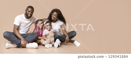 Portrait of happy african family with children sitting on floor on yellow studio background, free space 129341884