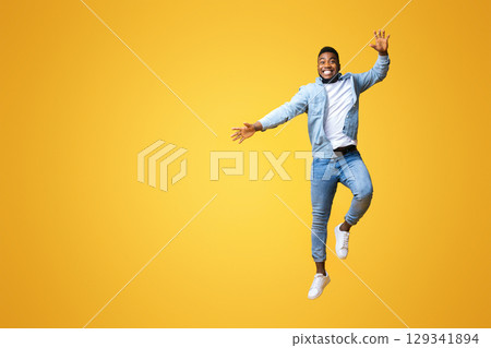 Cheerful millennial black guy having fun, jumping in air on yellow background, free space 129341894