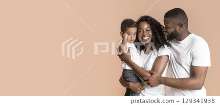 Family love. Portrait of young african american man and woman with their son on hands, yellow studio background with free space 129341938