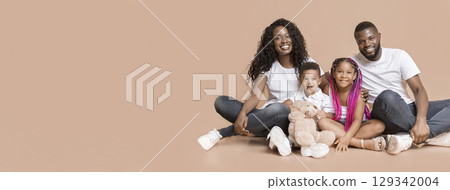 Family portrait. Happy mother and father with their children sitting on floor and posing to camera over yellow studio background Family portrait. Happy mother and father with their children sitting on floor and posing to camera over yellow studio background 129342004