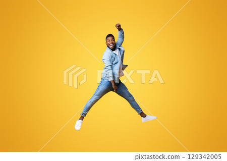 Full length of funny black guy jumping with raised arm against yellow studio background, copy space Full length of funny black guy jumping with raised arm against yellow studio background, copy space 129342005