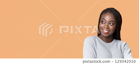 Interested pretty black woman in blue sweater looking at free space, panorama, beige background 129342010