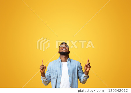 Look there. Handsome african american guy pointing upwards at copy space on yellow studio background. 129342012