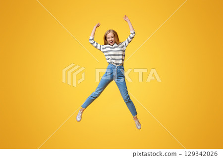 Carefree girl jumping with hands up, orange studio background 129342026