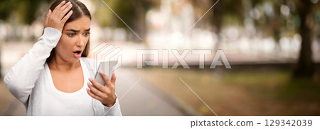 Bad News. Shocked Girl With Smartphone Reading Message Touching Head Standing In Park Outside 129342039