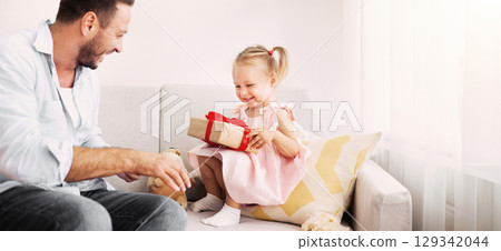 Birthday Girl. Excited daughter holding her present, happy father sitting nearby on the couch 129342044