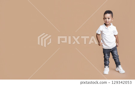Kid's fashion concept. Portrait of adorable little afro boy in jeans and white t-shirt standing on yellow background in studio, free space 129342053