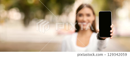Unrecognizable Woman Showing Cellphone Empty Screen Recommending Social Helpline Service Or App Standing Outdoor. Shallow Depth, Mockup Unrecognizable Woman Showing Cellphone Empty Screen Recommending Social Helpline Service Or App Standing Outdoor. Shallow Depth, Mockup 129342059
