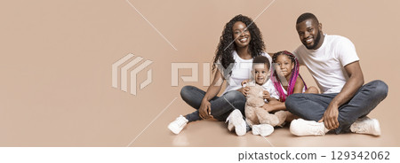 African American parents with daughter and son sitting together on floor and smiling over yellow studio background, panorama with copye space African American parents with daughter and son sitting together on floor and smiling over yellow studio background, panorama with copye space 129342062