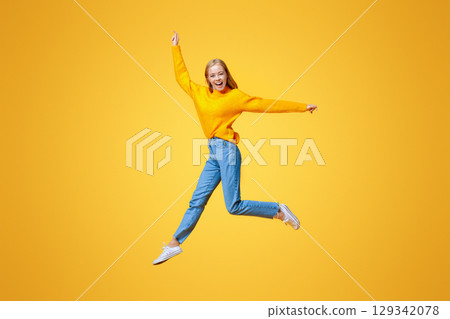 Jumping millennial girl in the air over orange studio background with free space Jumping millennial girl in the air over orange studio background with free space 129342078