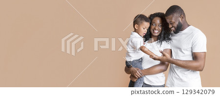 Portrait of african american mother, father and baby son bonding and posing in studio on yellow background, copy space Portrait of african american mother, father and baby son bonding and posing in studio on yellow background, copy space 129342079