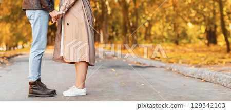 Lovers standing against each other and holding hands in public park in autumn, cropped, copy space 129342103