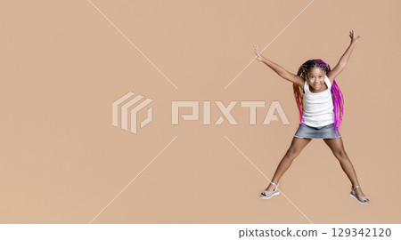 Like a star. Cute little african american girl jumping with her hands up over yellow studio background with copy space 129342120