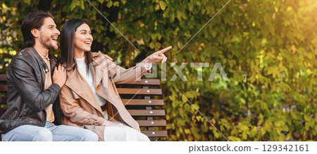 Emotional pretty girl showing something her boyfriend at park, pointing at copy space, panorama Emotional pretty girl showing something her boyfriend at park, pointing at copy space, panorama 129342161