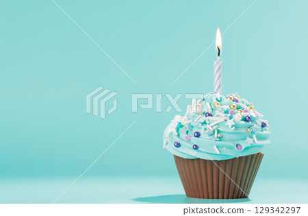 Festive cupcake topped with swirled frosting and a lit candle Festive cupcake topped with swirled frosting and a lit candle 129342297