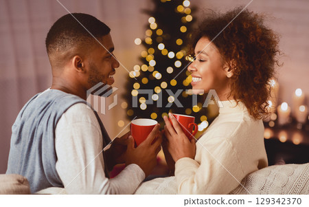 Excited black couple drinking coffee on Christmas eve, enjoying cozy evening at home 129342370
