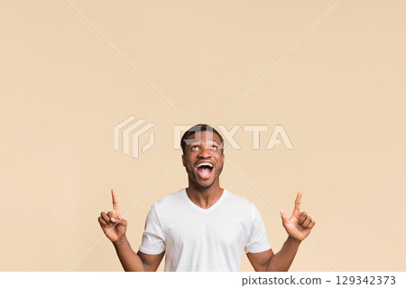 Look Up. Excited Black Guy Pointing Fingers Upward At Copy Space Standing Over Yellow Background In Studio. Look Up. Excited Black Guy Pointing Fingers Upward At Copy Space Standing Over Yellow Background In Studio. 129342373