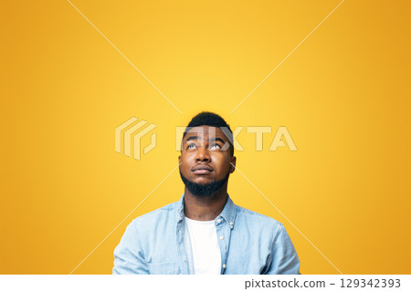 Doubtful african american man looking upwards at copy space on yellow background Doubtful african american man looking upwards at copy space on yellow background 129342393
