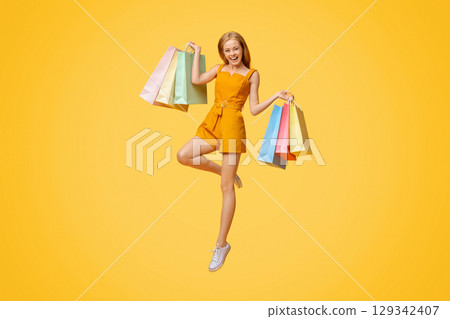 Happy Shopping. Overjoyed Blonde Girl With Bright Shopper Bags In Hand Jumping Over Yellow Background 129342407