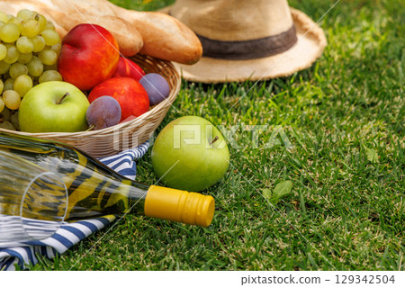 Picnic with wine, fruits, and baguette on a green meadow 129342504