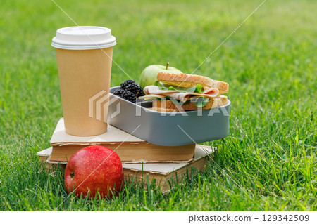 Picnic on a lawn with books, sandwiches, fruits, and coffee 129342509