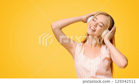 Favorite Leisure. Cheerful Teen Girl In Wireless Headphones Listening Music, Enjoying Songs With Closed Eyes, Standing On Yellow Background, Free Space 129342511