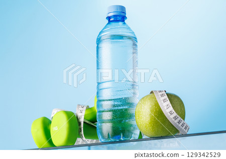 Bottle of water, green apple, and dumbbells on a glass table Bottle of water, green apple, and dumbbells on a glass table 129342529