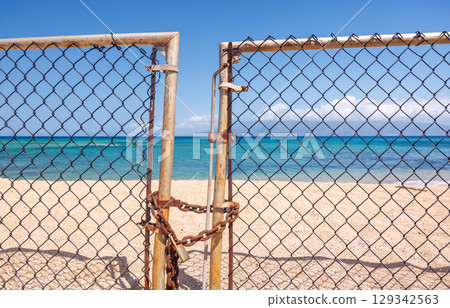 Beach entrance closed with a metal fence and lock in the foreground 129342563