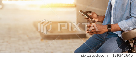 Modern Outdoor Leisure. Unrecognizable african man leaning on bicycle, using smartphone and drinking takeaway coffee outside 129342649