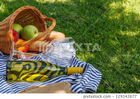 Picnic basket with wine, fruits, and baguette on a sunny green meadow Picnic basket with wine, fruits, and baguette on a sunny green meadow 129342677