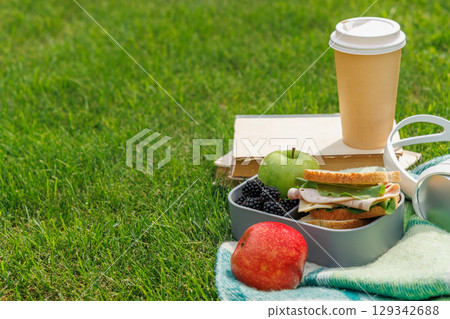 Picnic on a lawn with books, sandwiches, fruits, and coffee 129342688