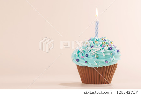 Festive cupcake topped with swirled frosting and a lit candle Festive cupcake topped with swirled frosting and a lit candle 129342717