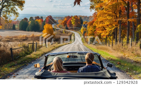A couple enjoys a leisurely drive down a winding country road surrounded by colorful autumn leaves. 129342928