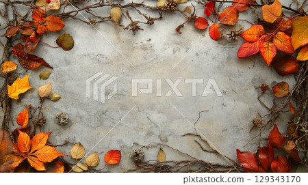 Colorful autumn leaves and twigs create a decorative border around a blank, textured surface, illuminated softly. 129343170