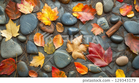 Vibrant autumn leaves in shades of red, orange, and yellow lay atop smooth pebbles, creating a beautiful natural display. 129343179
