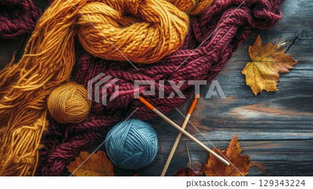 A vibrant display of yarn balls, knitting needles, and autumn leaves arranged on a rustic wooden surface, inviting creativity and warmth. 129343224