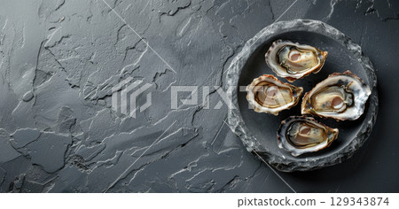 A plate holds four freshly shucked oysters, presented on a textured slate surface, showcasing their natural beauty and freshness. 129343874
