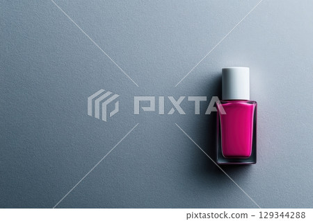 Bright pink nail polish bottle on a smooth grey surface showcasing vibrant color 129344288