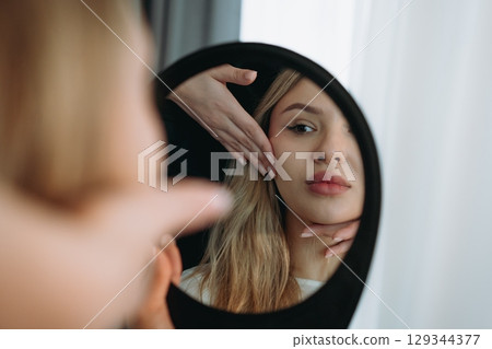 young woman looking in a mirror after facian rejuvenation procedure at aesthetic clinic  129344377