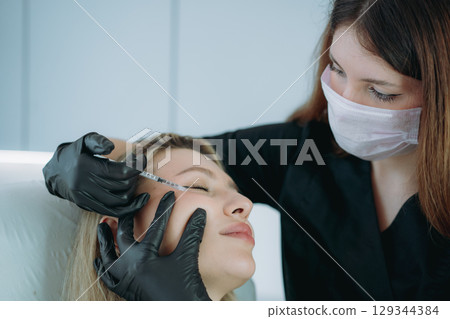 an aesthetic professional performing an injection procedure. Beauty treatment 129344384