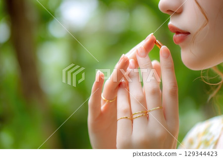 cropped portrait of young asian girl hoding a capsule or pill near lips on natural green background 129344423