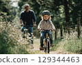 child in helmet riding a bicycle without assiastance in summer park. Father cycling behind. Run a bike day 129344463