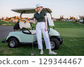 young woman lstands against a vintage golf cart wearing relaxed golfcore outfit 129344467