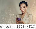 asian young woman with fresh glowing skin holding a small deep purple cosmetic jar without label 129344513