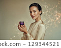 asian young woman with fresh glowing skin holding a small deep purple cosmetic jar without label 129344521